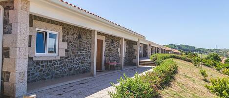 A row of stone buildings with a covered walkway, outdoor seating, and a view of the countryside.