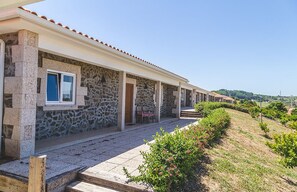 A row of stone buildings with a covered walkway, outdoor seating, and a view of the countryside.