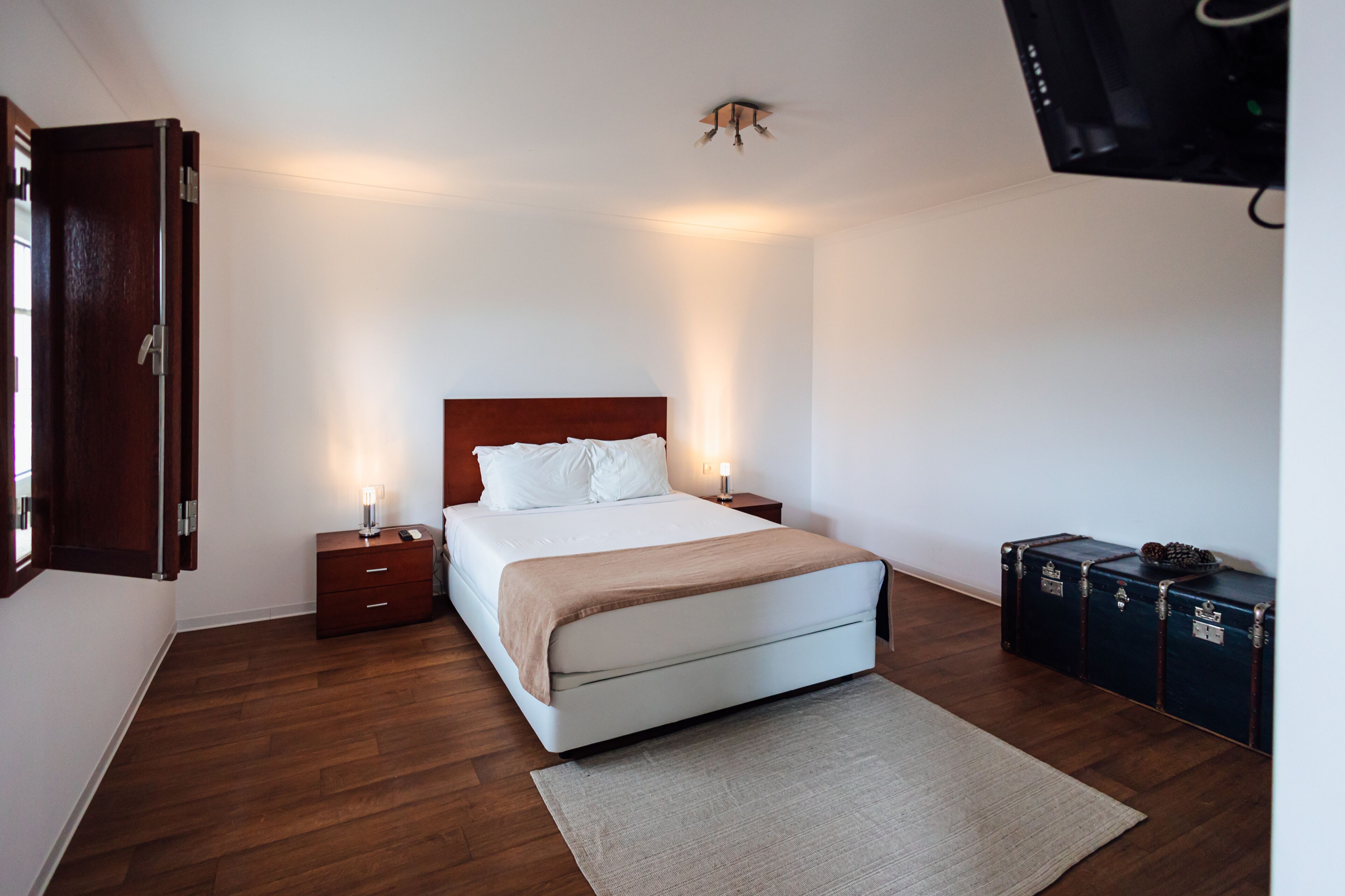Una habitación de hotel con cama, mesitas de noche, televisor en la pared y una maleta en el suelo.