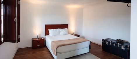 Una habitación de hotel con cama, mesitas de noche, televisor en la pared y una maleta en el suelo.