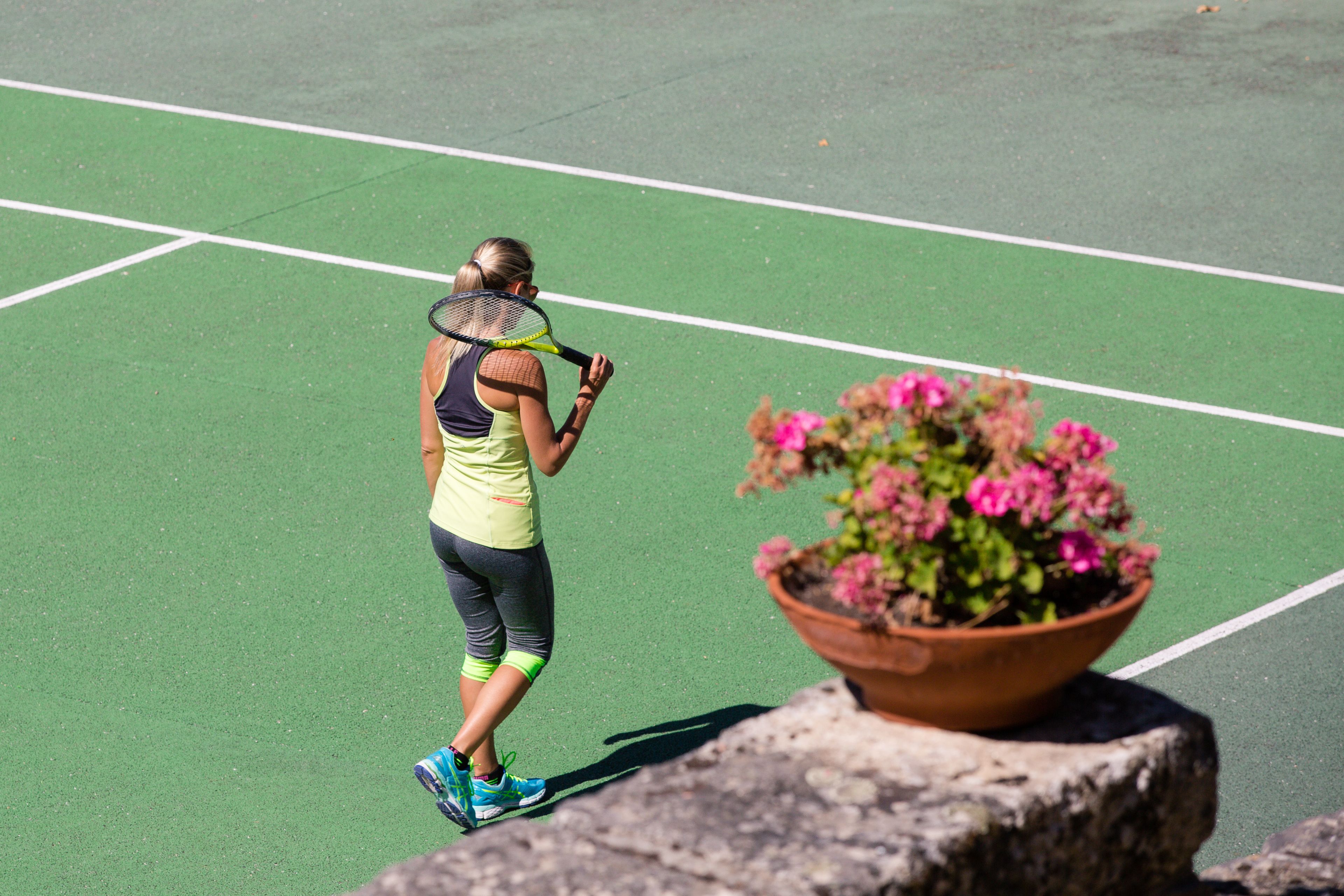 Ein Tennisspieler auf einem grünen Platz, in der Nähe ein Blumentopf.