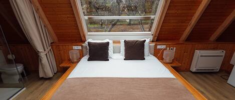 A bedroom with a large bed, wooden walls, a window with a view of trees, and a built-in heater.