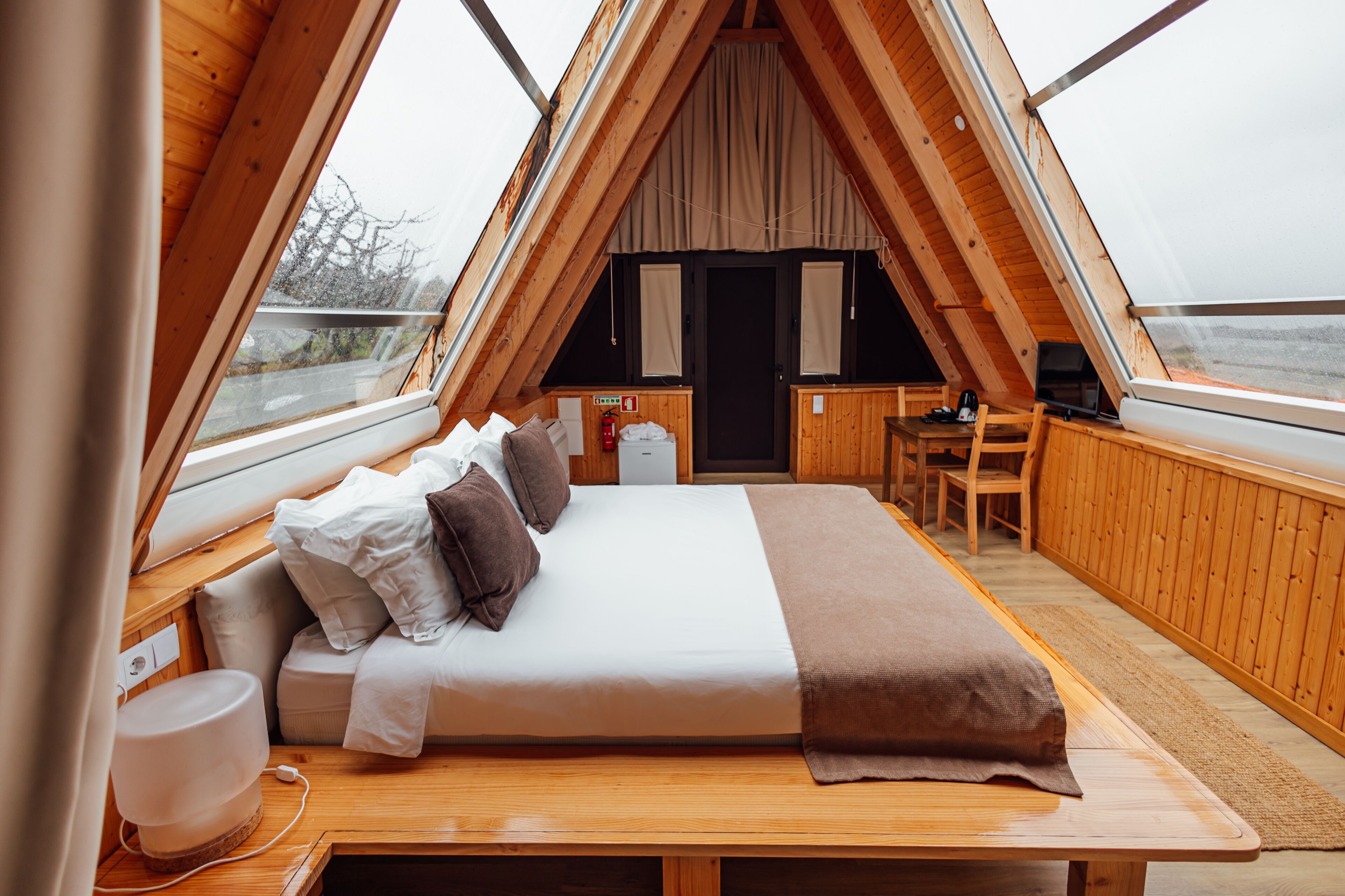 Una habitación de madera acogedora y triangular con una cama, un escritorio y una silla.