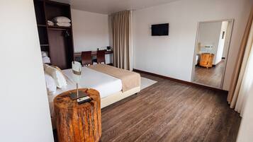 Habitación de hotel con cama, mesita de noche, mesita auxiliar de madera y un televisor fijado a la pared.
