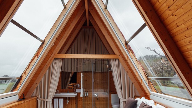 A triangular wooden room with a bed, a bathroom, and large windows. - Quinta da Barroca (Armamar)