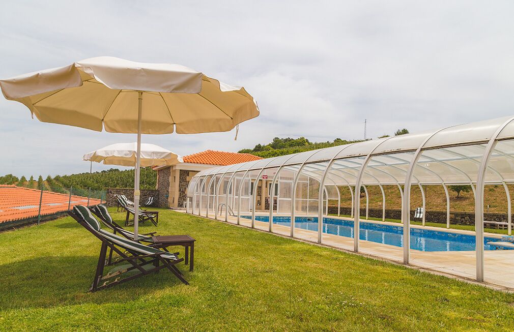 A pool area with lounge chairs and umbrellas, a greenhouse structure, and a swimming pool.