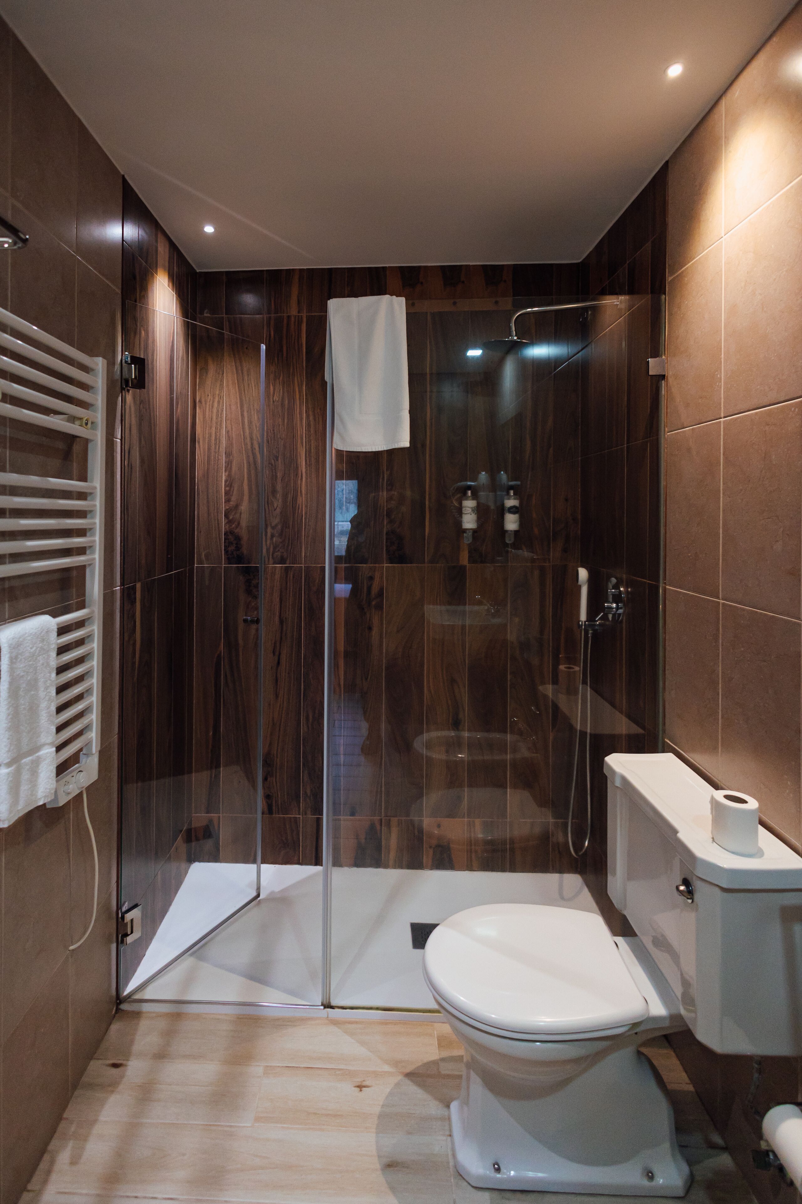 A modern bathroom with a glass-enclosed shower, a toilet, and a towel rack.