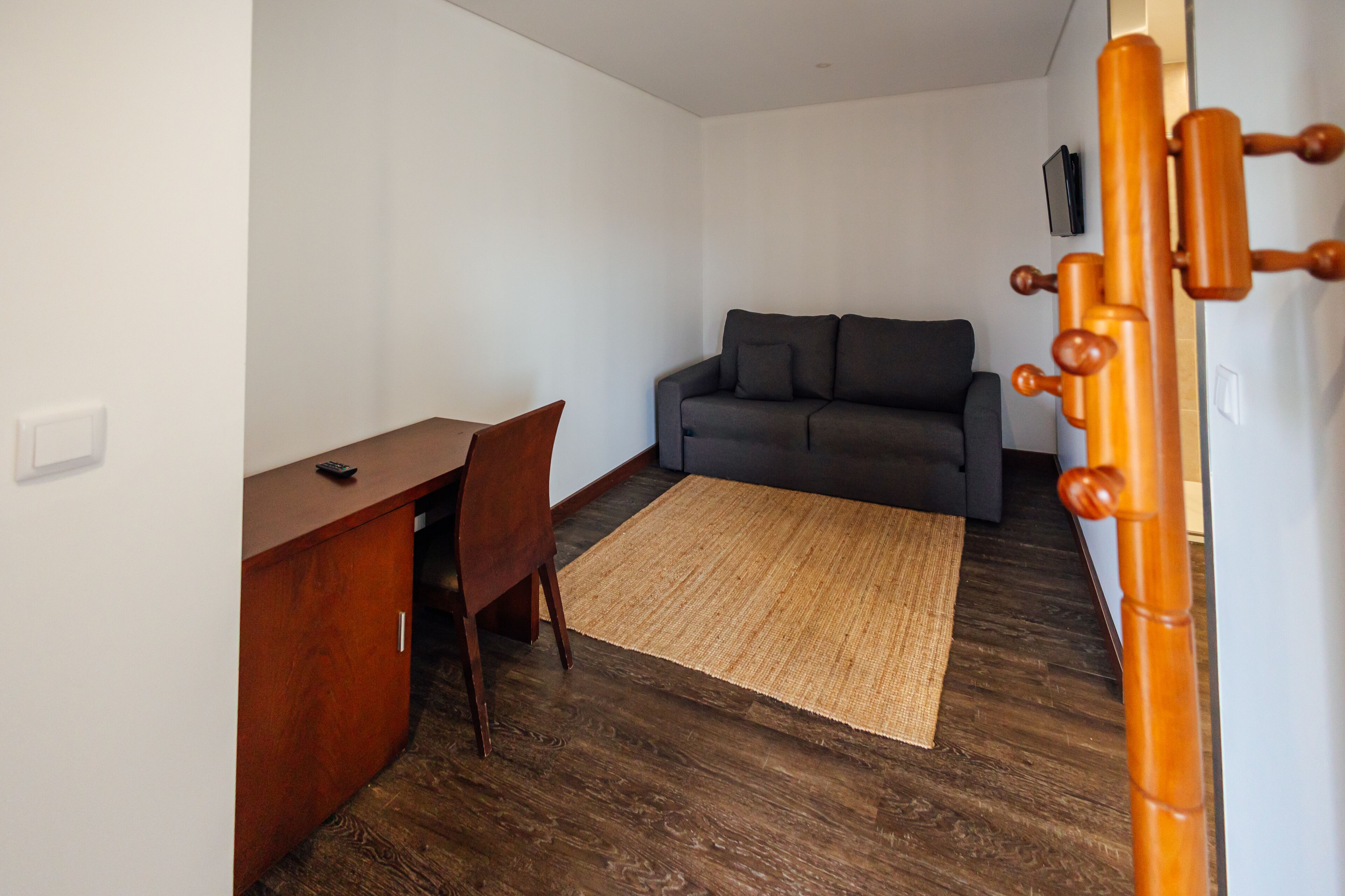 A room with a wooden desk, a grey sofa, and a woven rug on a wooden floor.