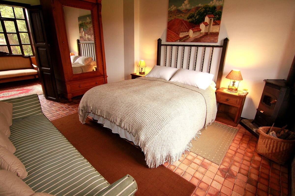 A bedroom with a bed, a wooden headboard, a nightstand with a lamp, a bench, and a painting on the wall.