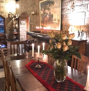 A dining table with a vase of roses, candles, and a plaid placemat.