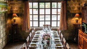 A long dining table set for a meal in a stone-walled room with a view of the outdoors. - Hacienda Hato Verde (Latacunga)