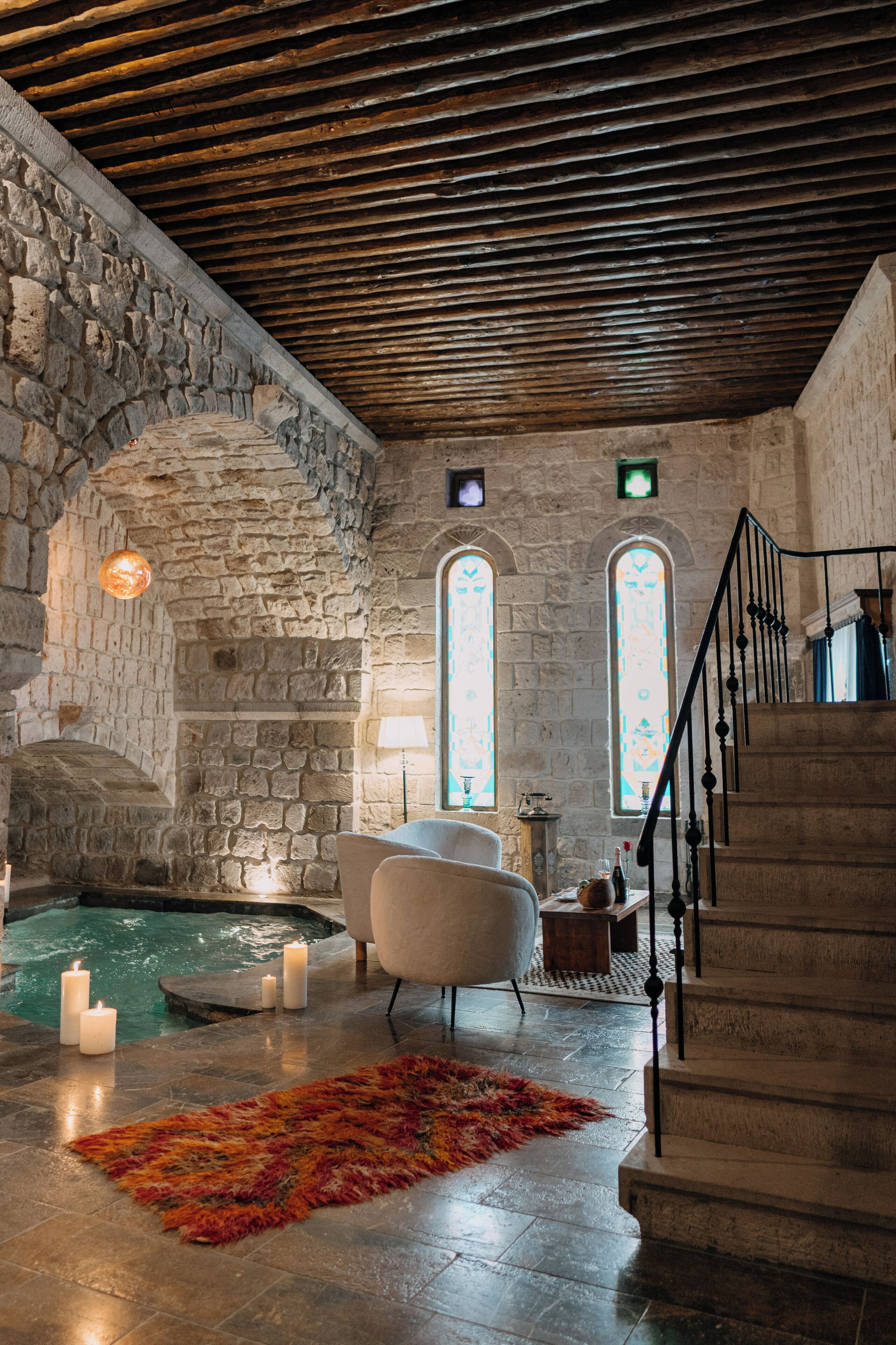 A stone-walled room with a stone staircase, a small pool, and a white armchair.