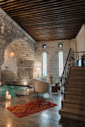 A stone-walled room with a stone staircase, a small pool, and a white armchair. - MUSEUM HOTEL - Relais & Châteaux (Nevsehir)