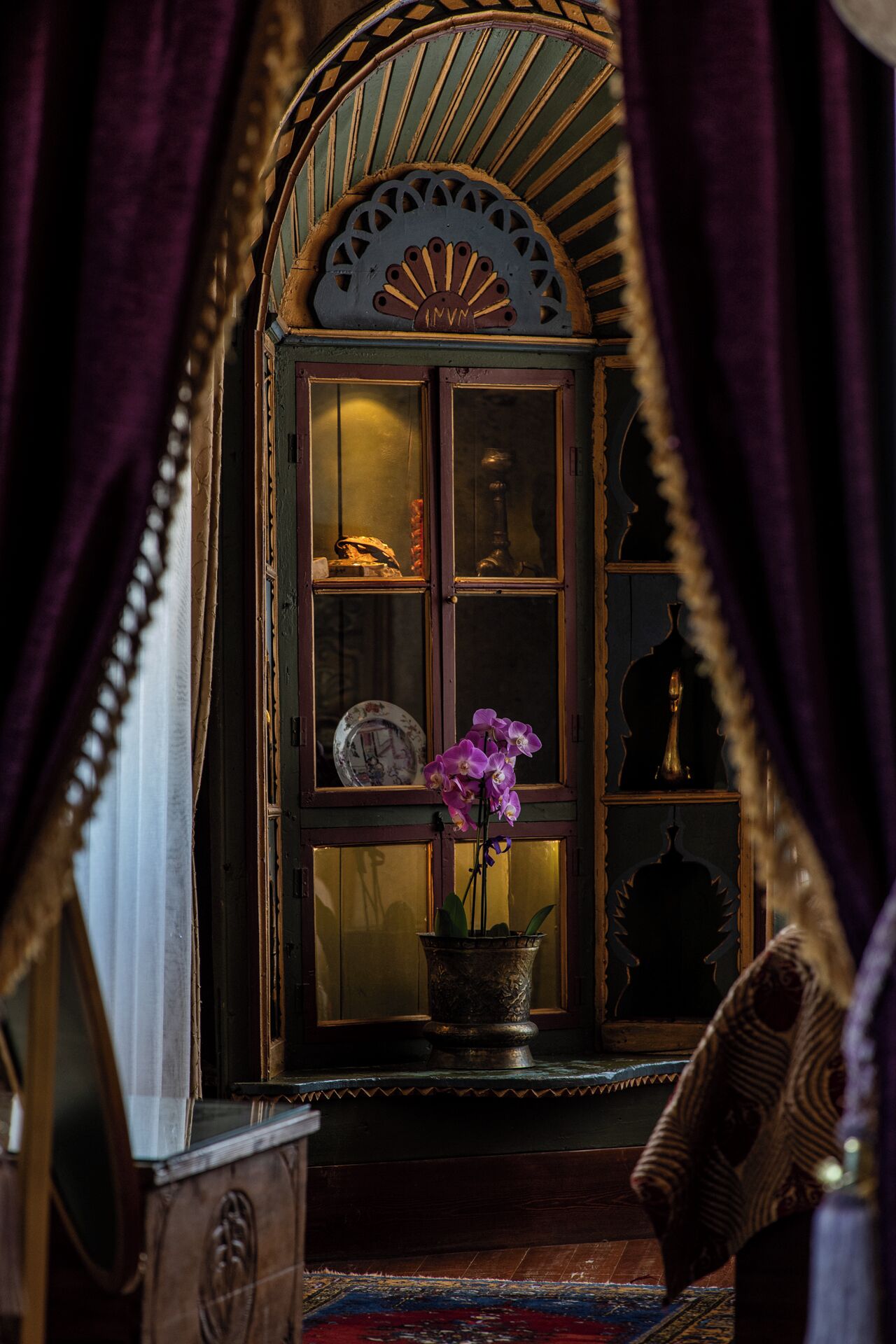 Een kamer met een houten kast, daarin een klok, een vaas met bloemen en decoratieve objecten.
