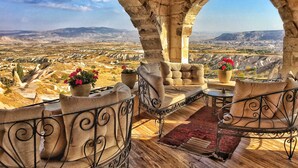 Un balcón con arcos de piedra, vistas de un valle y plantas en macetas.