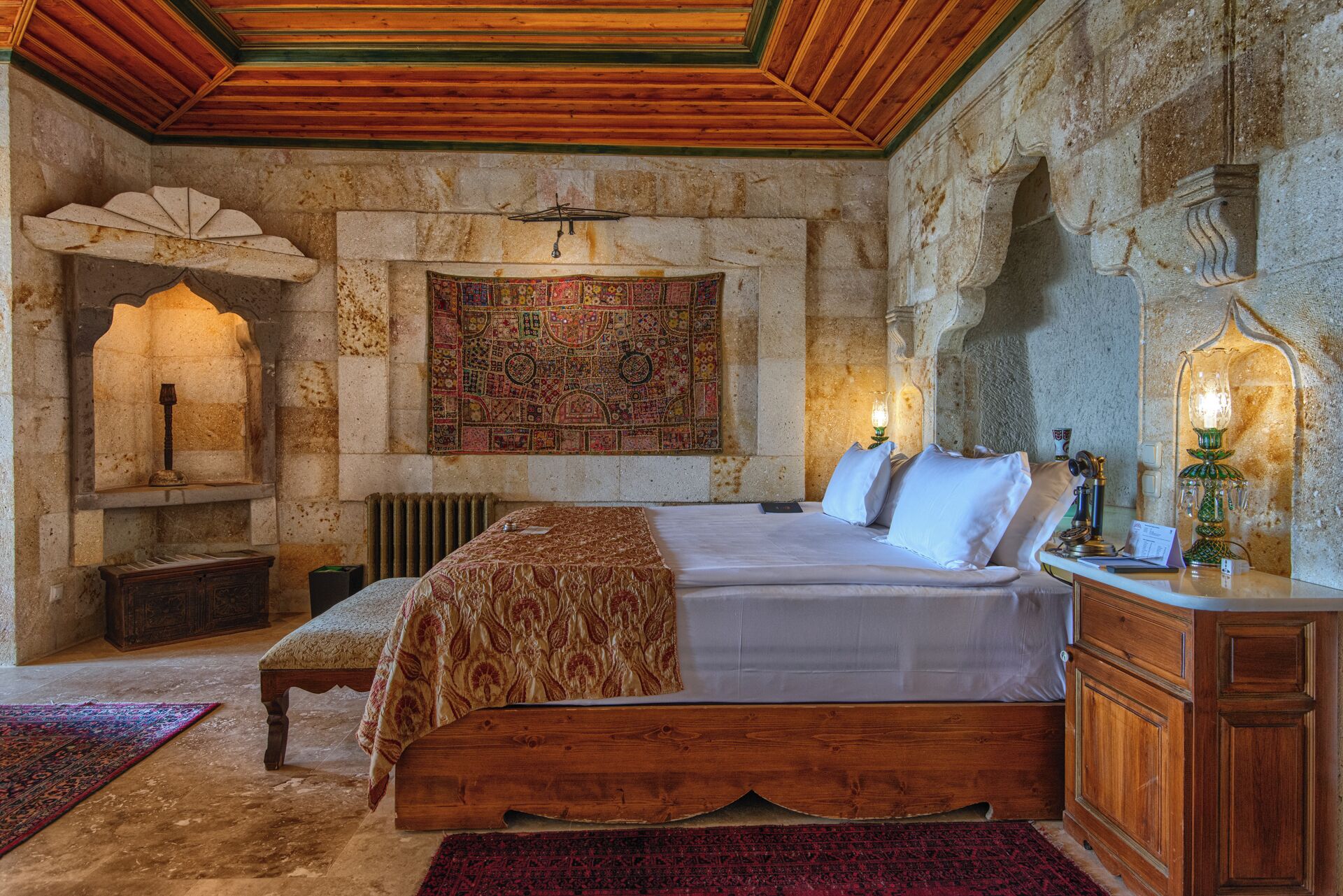 A traditional room with a bed, wooden furniture, a stone wall, and a decorative tapestry.
