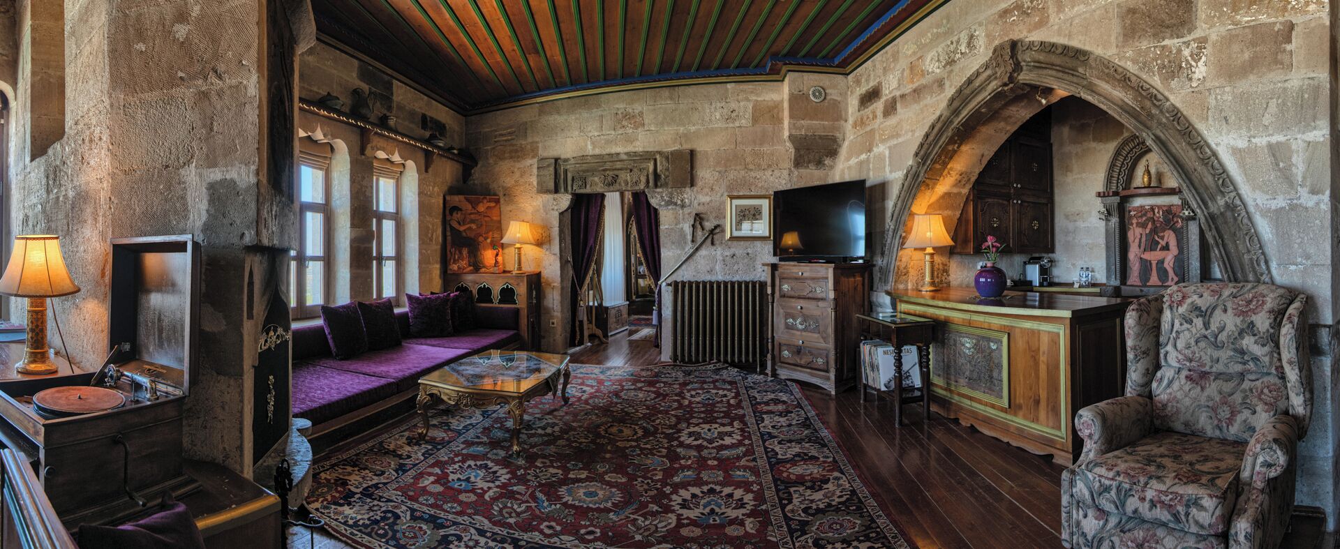 A cozy room with a wooden ceiling, stone walls, a sofa, a television, and a fireplace.