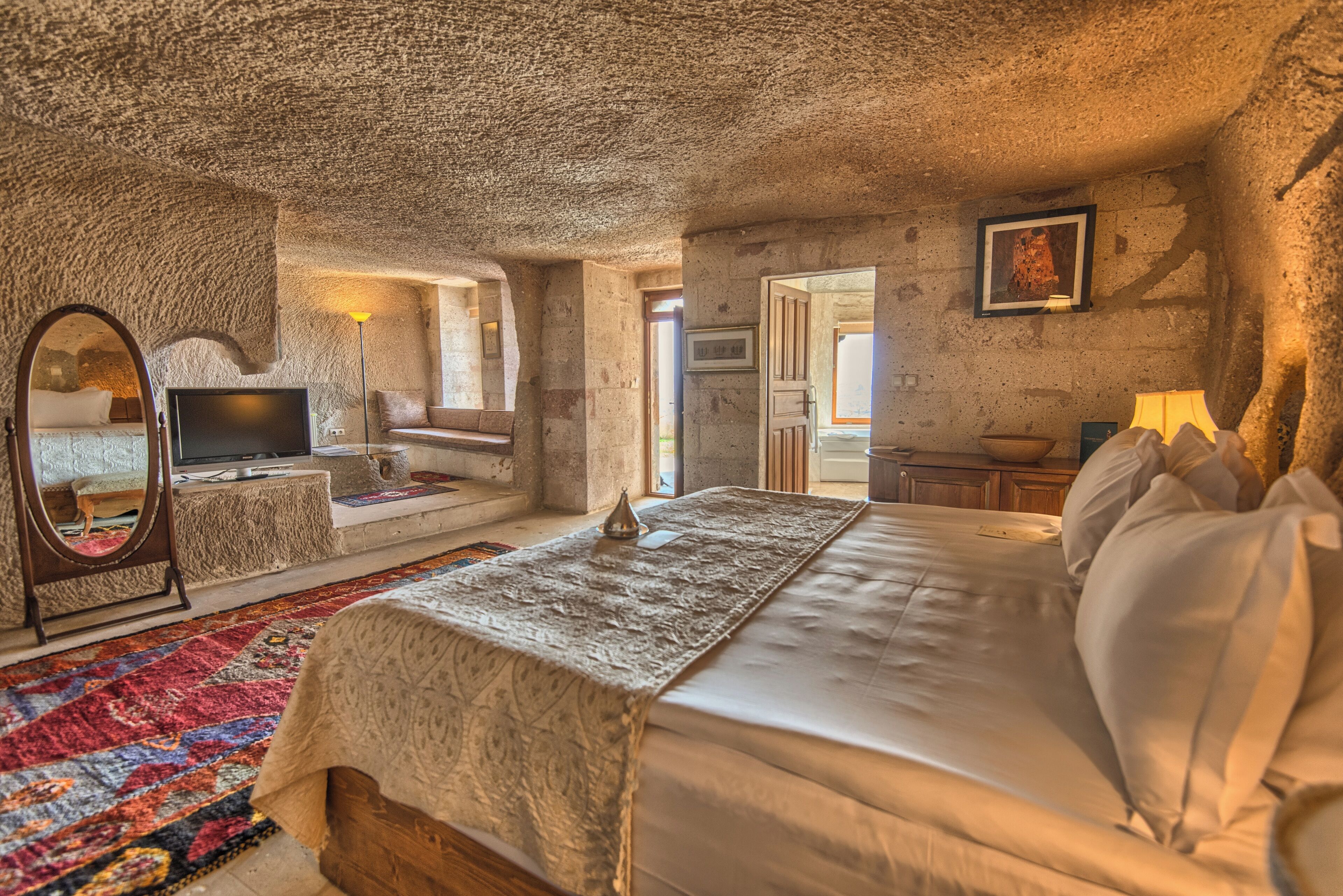 Een gezellige slaapkamer met een stenen plafond, een groot bed, een televisie en een spiegel.