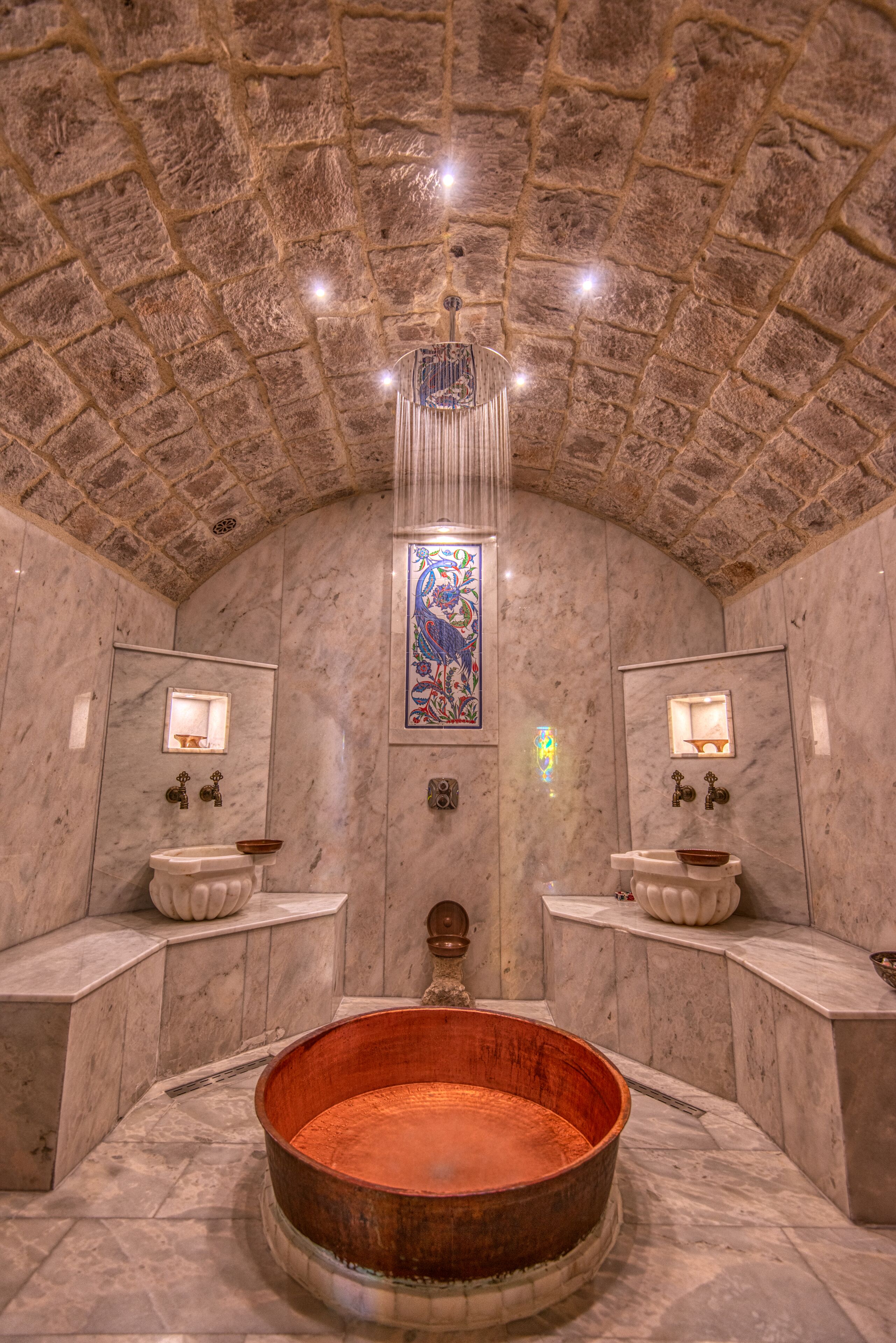 Un baño con un lavabo grande de cobre, paredes de piedra y una ventana con vitral.
