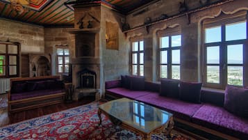 A traditional room with a stone fireplace, a sofa with cushions, a glass-top table, and large windows with a view.