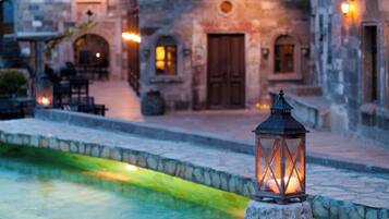 A stone lantern on a cobblestone path with a pool and stone buildings in the background.