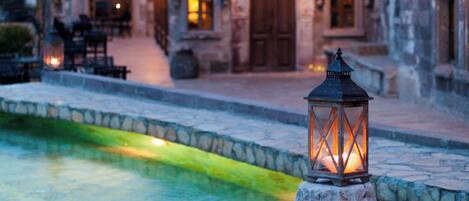 A stone lantern on a cobblestone path with a pool and stone buildings in the background.