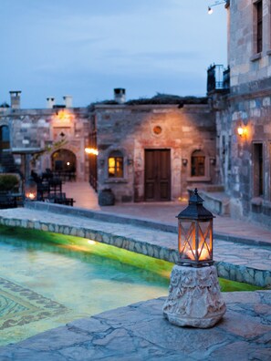 A stone lantern on a cobblestone path with a pool and stone buildings in the background. - MUSEUM HOTEL - Relais & Châteaux (Nevsehir)