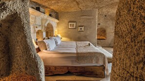 A stone-walled bedroom with a bed, pillows, and a wooden bench. - MUSEUM HOTEL - Relais & Châteaux (Nevsehir)