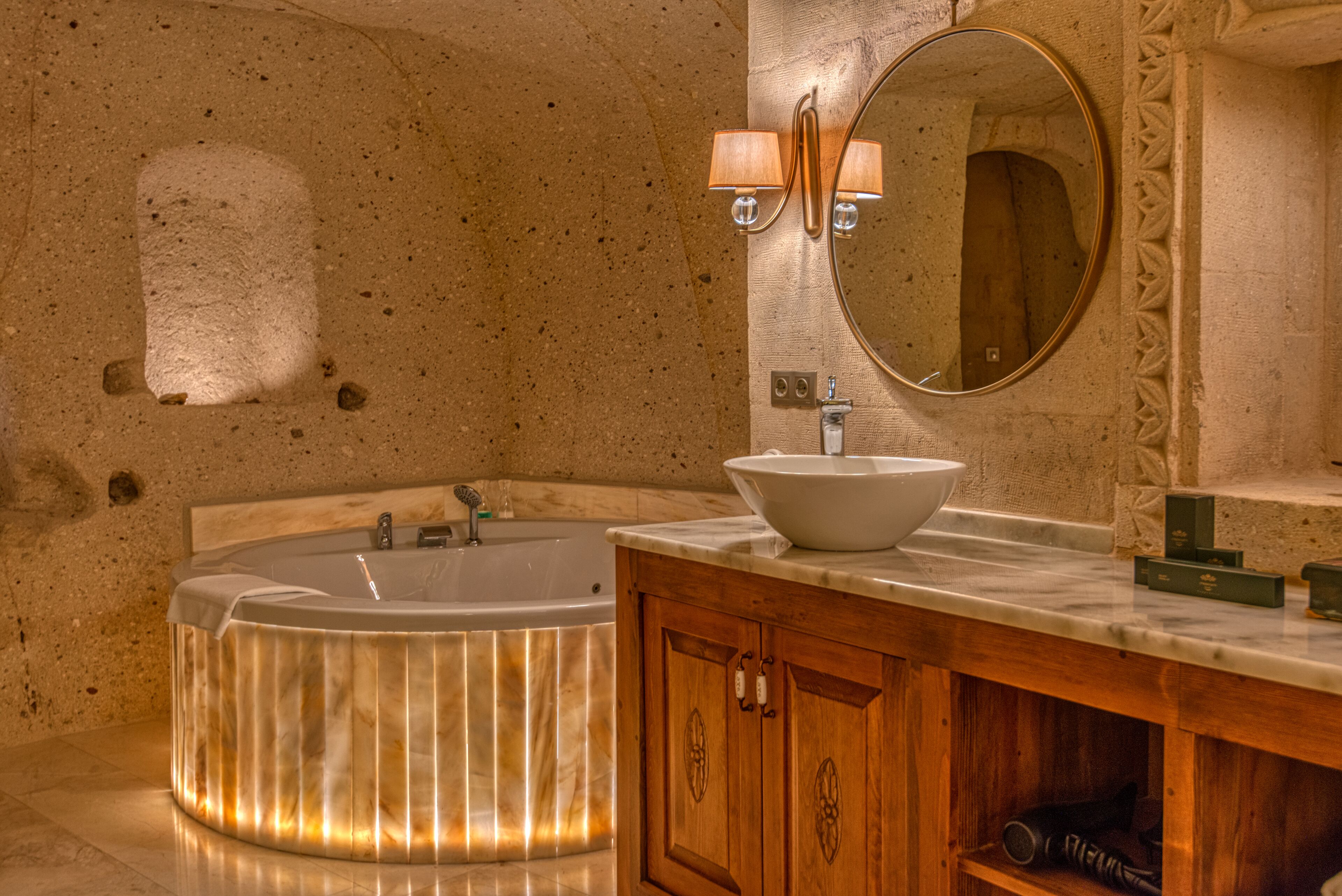 A modern bathroom with a freestanding bathtub, a vanity with a large mirror, and a stone wall.