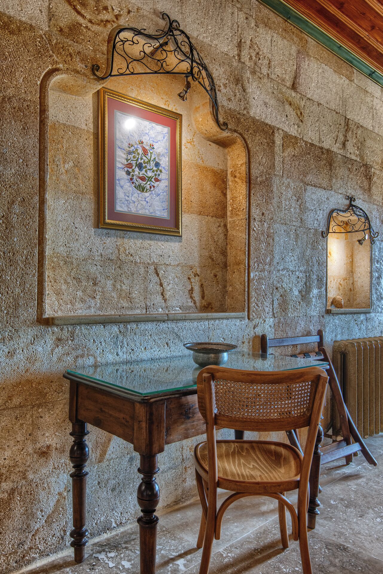 A rustic room with a stone wall, a wooden chair, a table, and a framed picture.