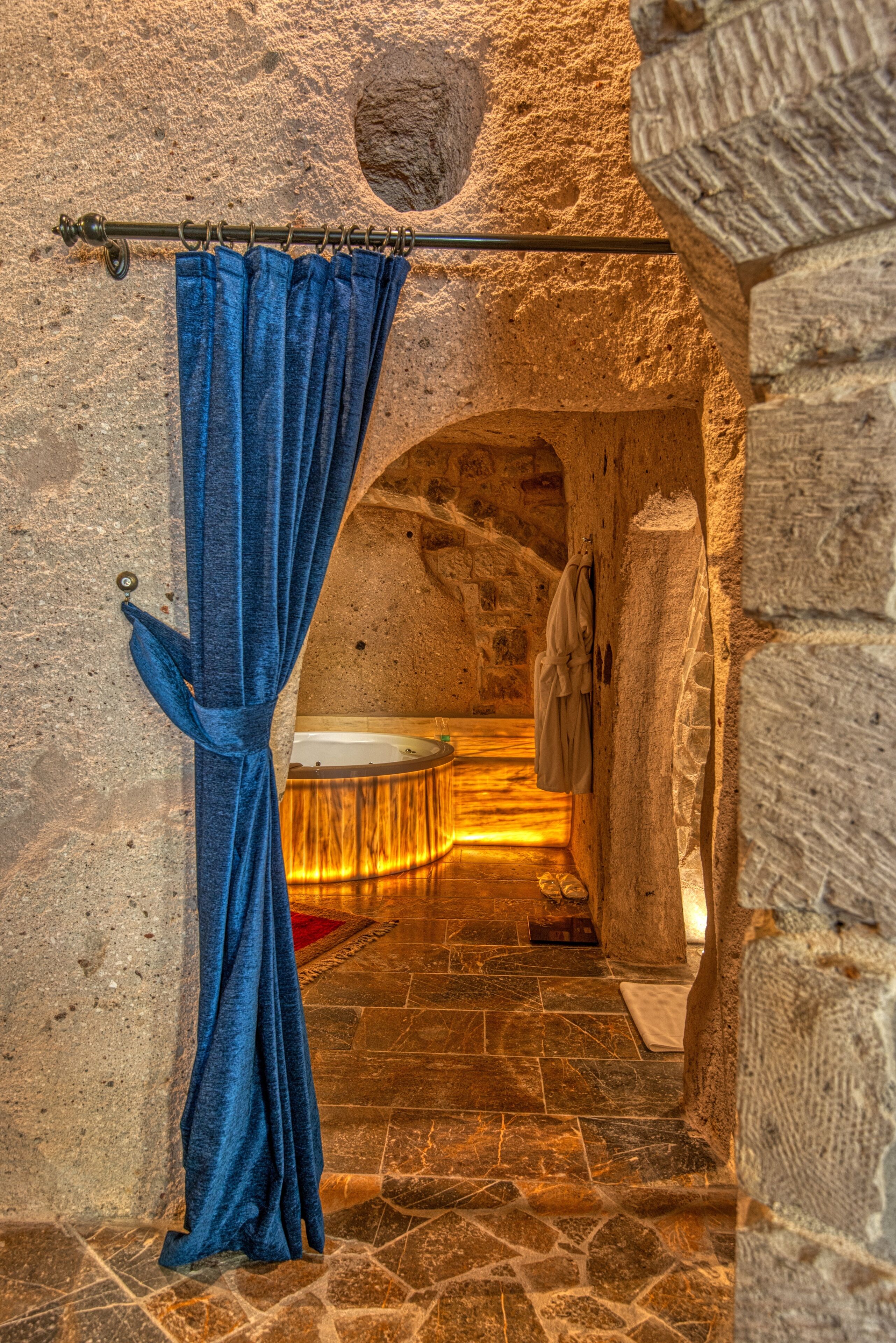 Un bagno con pareti in pietra, una vasca, un portascopino e una tenda blu.