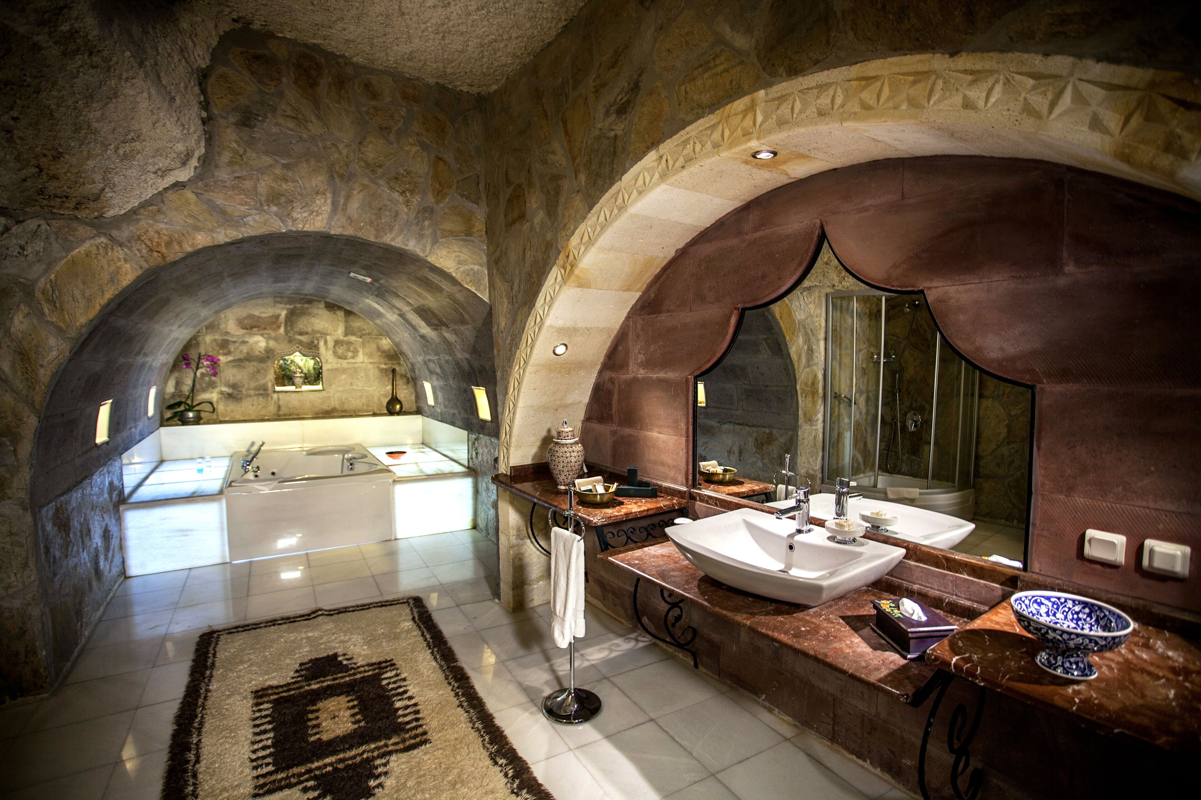 A luxurious bathroom with a large arched mirror, a bathtub, and a double sink.