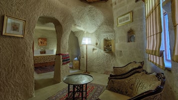 A room with a stone wall, a bed, a table, and a sofa. There are framed pictures on the wall and a lamp on the table.