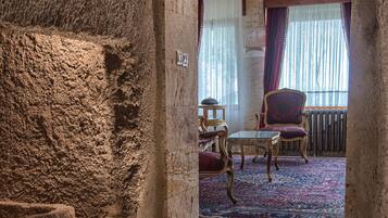 Un pasillo con paredes de piedra que conduce a una habitación con alfombra estampada, un candelabro y una ventana con cortinas.