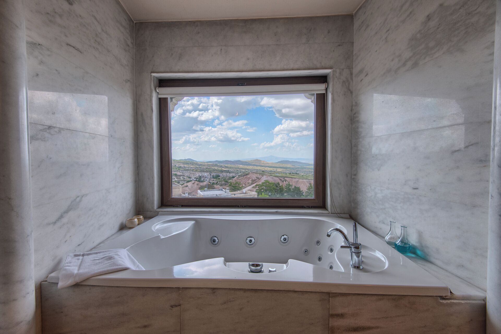 A bathroom with a large bathtub, a window with a view of a landscape, and marble walls.