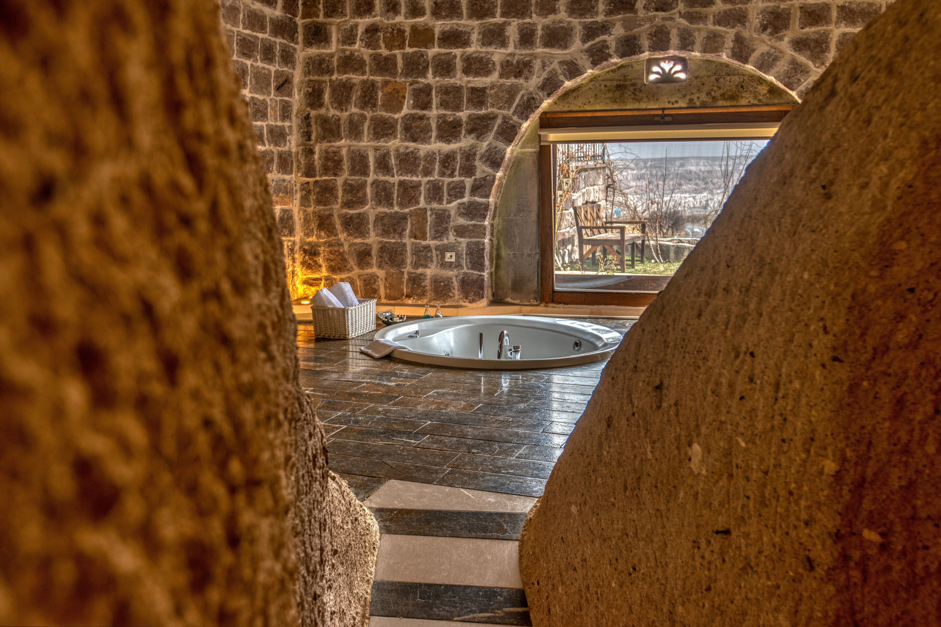 Ein Badezimmer mit Stebwänden und Steinboden, einer Badewanne und einem Fenster mit Blick nach draußen.