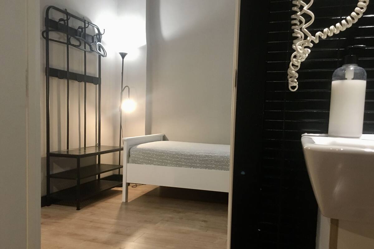 Un dormitorio pequeño y ordenado con una cama individual, una mesita de noche, una lámpara y un radiador.