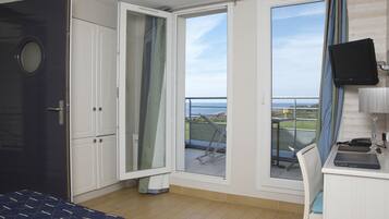 Una habitación con cama, escritorio con una computadora portátil, televisor y puerta corrediza de vidrio a un balcón con vistas.