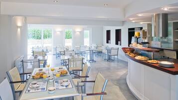 Un vaste espace dédié à la restauration, avec de nombreuses tables et chaises, un buffet proposant une variété de plats et de boissons, et de grandes fenêtres laissant entrer la lumière naturelle.