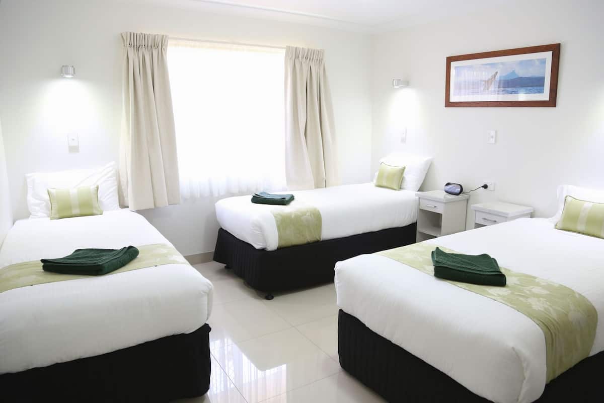 Habitación de hotel con tres camas, un escritorio y un cuadro en la pared.