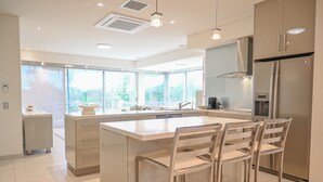 A modern kitchen with a large island, bar stools, and a stainless steel refrigerator. - Bay Motel (Byron Bay)