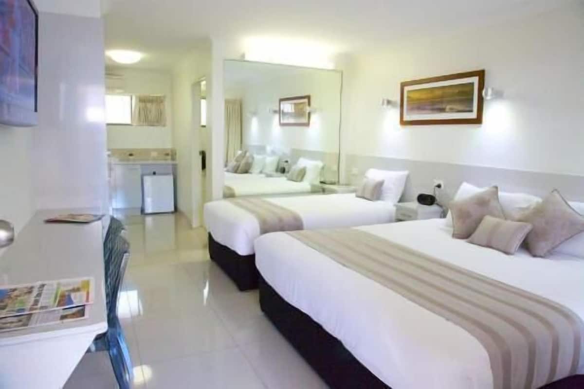 Habitación de hotel con dos camas, un escritorio, un espejo y una pequeña kitchenette.