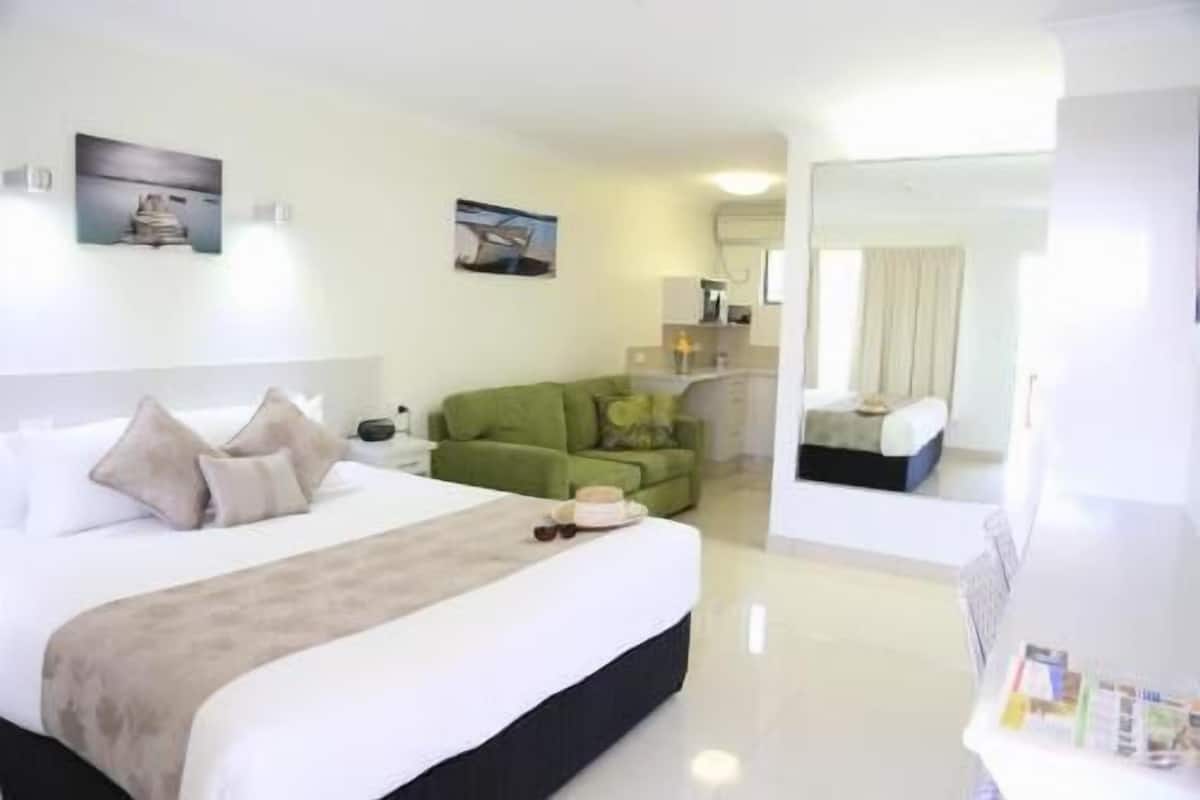 Una habitación de hotel con una cama, un sofá verde, una mesita con una taza y un espejo.
