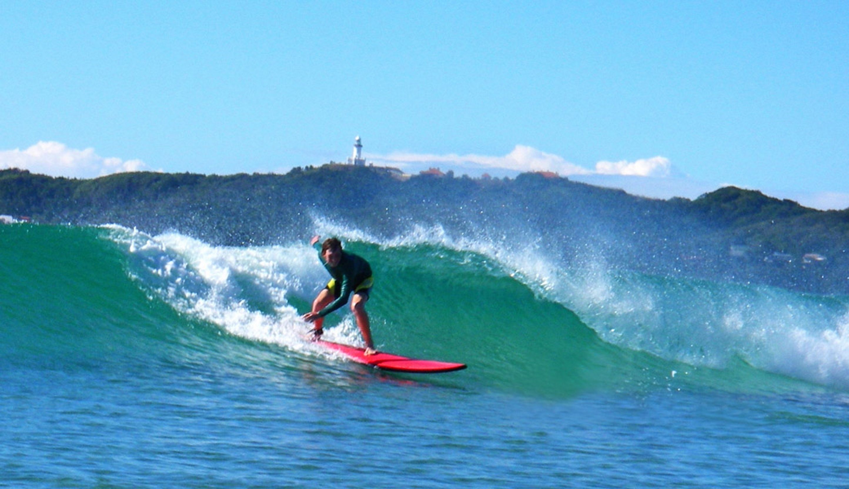 Una persona surfeando una ola, con un faro al fondo.
