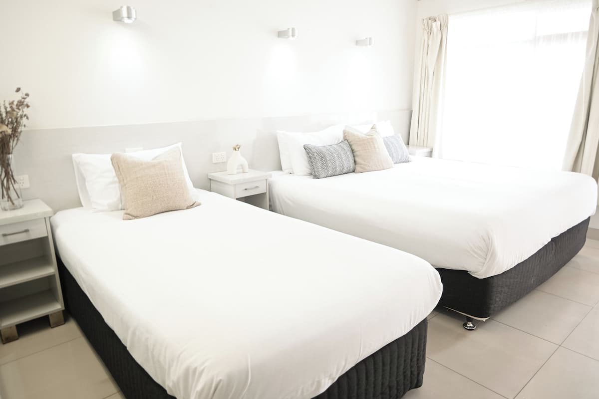 Habitación de hotel con dos camas, una mesita de noche, un jarrón con flores y una ventana con cortinas.