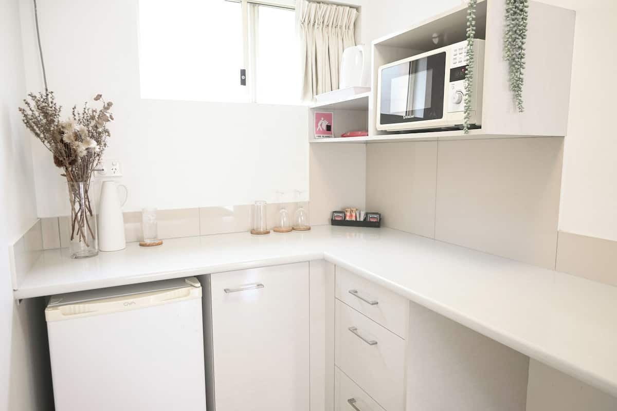 Una cocina con armarios blancos, un microondas y un ventanal con cortinas.