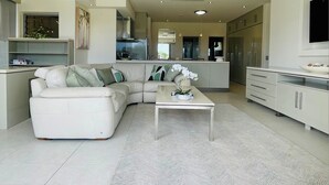 A modern living room with a sofa and a coffee table, a kitchen area with cabinets and appliances, and a flat-screen TV mounted on the wall. - Bay Motel (Byron Bay)