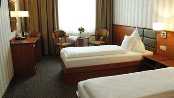 Ein Hotelzimmer mit zwei Betten, einem Schreibtisch mit Lampe, einem Stuhl und einem kleinen Tisch mit Blumen.
