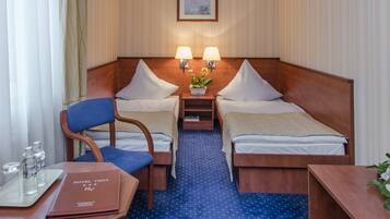 Hotelkamer met twee enkele bedden, een houten nachtkastje met lampen, een stoel, een klein tafeltje met een dienblad vol waterflessen en een blauw tapijt.