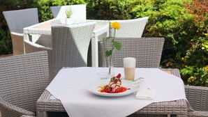 A dining table with a white tablecloth, a plate of food, a glass of beverage, and a vase with a single yellow flower. - Business Hotel Vega (Wroclaw)